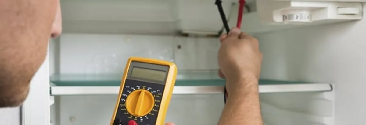 Refrigerator repair technician testing electrical components with a multimeter in Wichita, KS